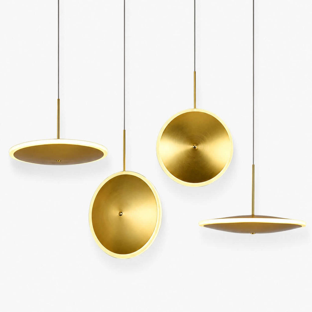Four Clérachic brushed gold disc pendants in horizontal and vertical styles hang at different heights on a plain white backdrop, each with a glowing edge.