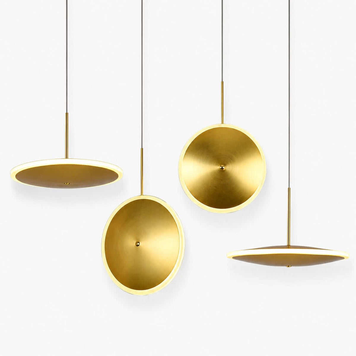 Four Clérachic brushed gold disc pendants in horizontal and vertical styles hang at different heights on a plain white backdrop, each with a glowing edge.