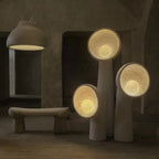 Three lit Clérachic floor lamps of different heights glowing warm inside their bowl shades, with a stone-textured bench and hanging dome light beyond.