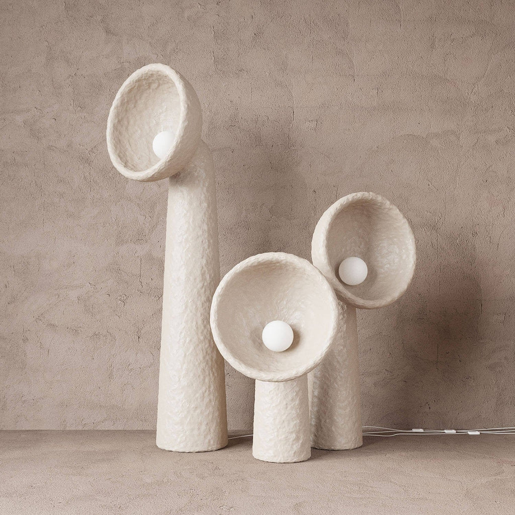 Three white textured Clérachic floor lamps of different heights against a soft taupe plaster wall, their round bulbs sitting in the bowls.