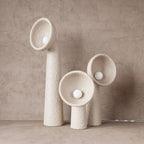 Three white textured Clérachic floor lamps of different heights against a soft taupe plaster wall, their round bulbs sitting in the bowls.