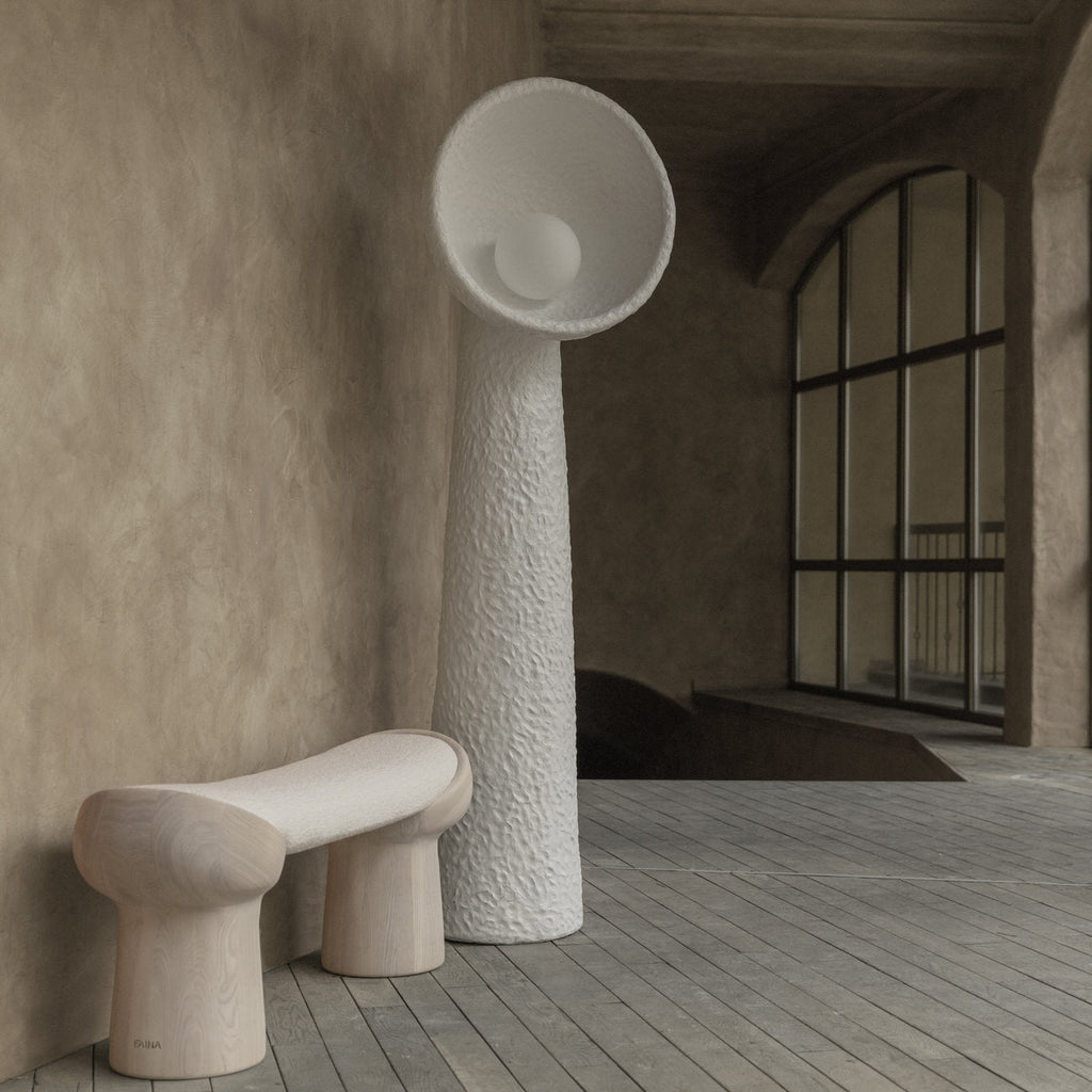 White textured Clérachic floor lamp beside a chunky stone-look bench, in a plaster room with an arched black-framed window.
