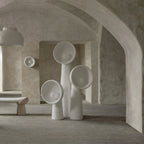 Three white Clérachic floor lamps of different heights in a vaulted plaster room, with a bench and a small wall light behind.