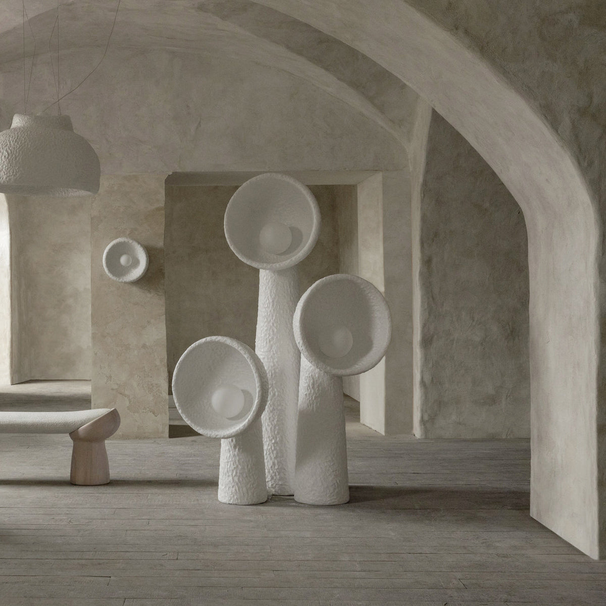 Three white Clérachic floor lamps of different heights in a vaulted plaster room, with a bench and a small wall light behind.