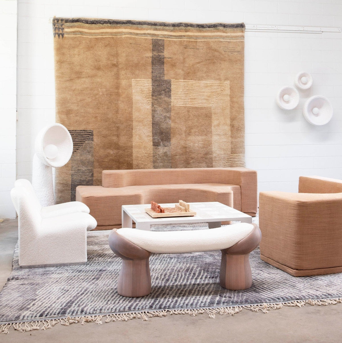 White Clérachic floor lamp at the back of a lounge with a pale armchair, a pink-toned sofa and a rug on the wall.