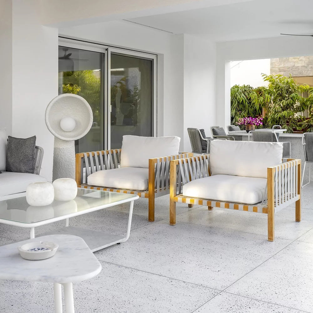 White Clérachic floor lamp in a terrace room with teak-framed armchairs, a glass coffee table and a marble side table.