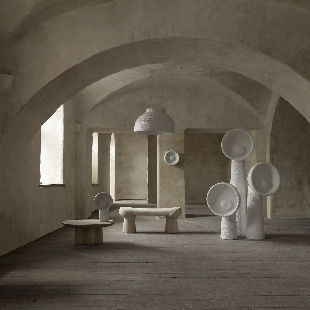 Vaulted plaster room with a group of Clérachic floor lamps, a low bench and a round table in the background.
