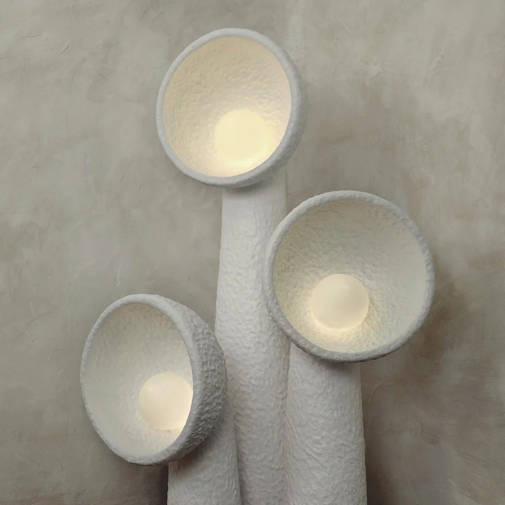 Close view of three Clérachic floor lamps lit from within, warm light glowing inside each rough-textured white bowl shade.