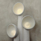 Close view of three Clérachic floor lamps lit from within, warm light glowing inside each rough-textured white bowl shade.