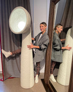 Person standing beside a tall white Clérachic floor lamp, showing its height against a curtain and a mirror.