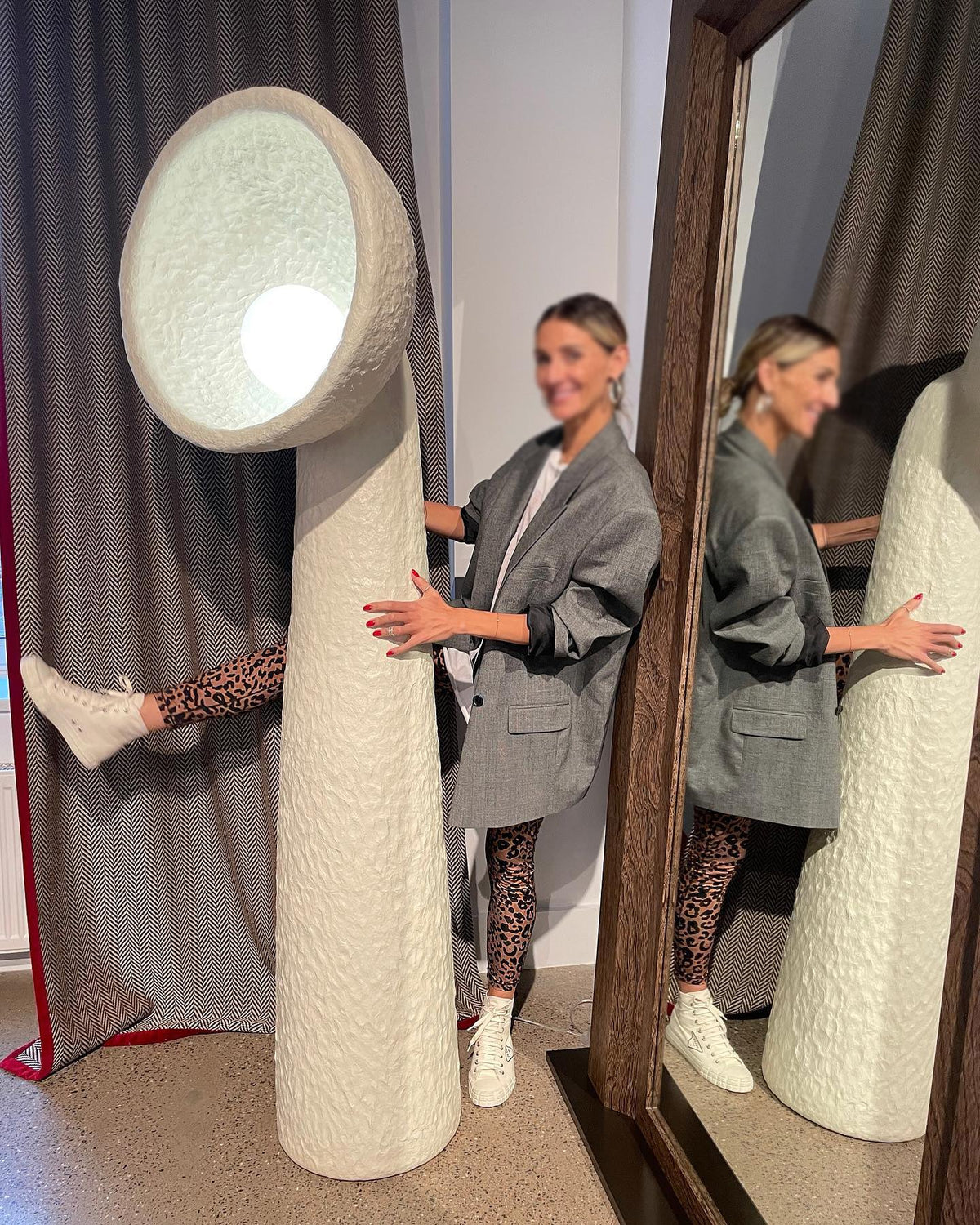 Person standing beside a tall white Clérachic floor lamp, showing its height against a curtain and a mirror.