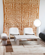 White Clérachic floor lamp beside a pair of white armchairs and a square coffee table, with a large woven rug on the wall.