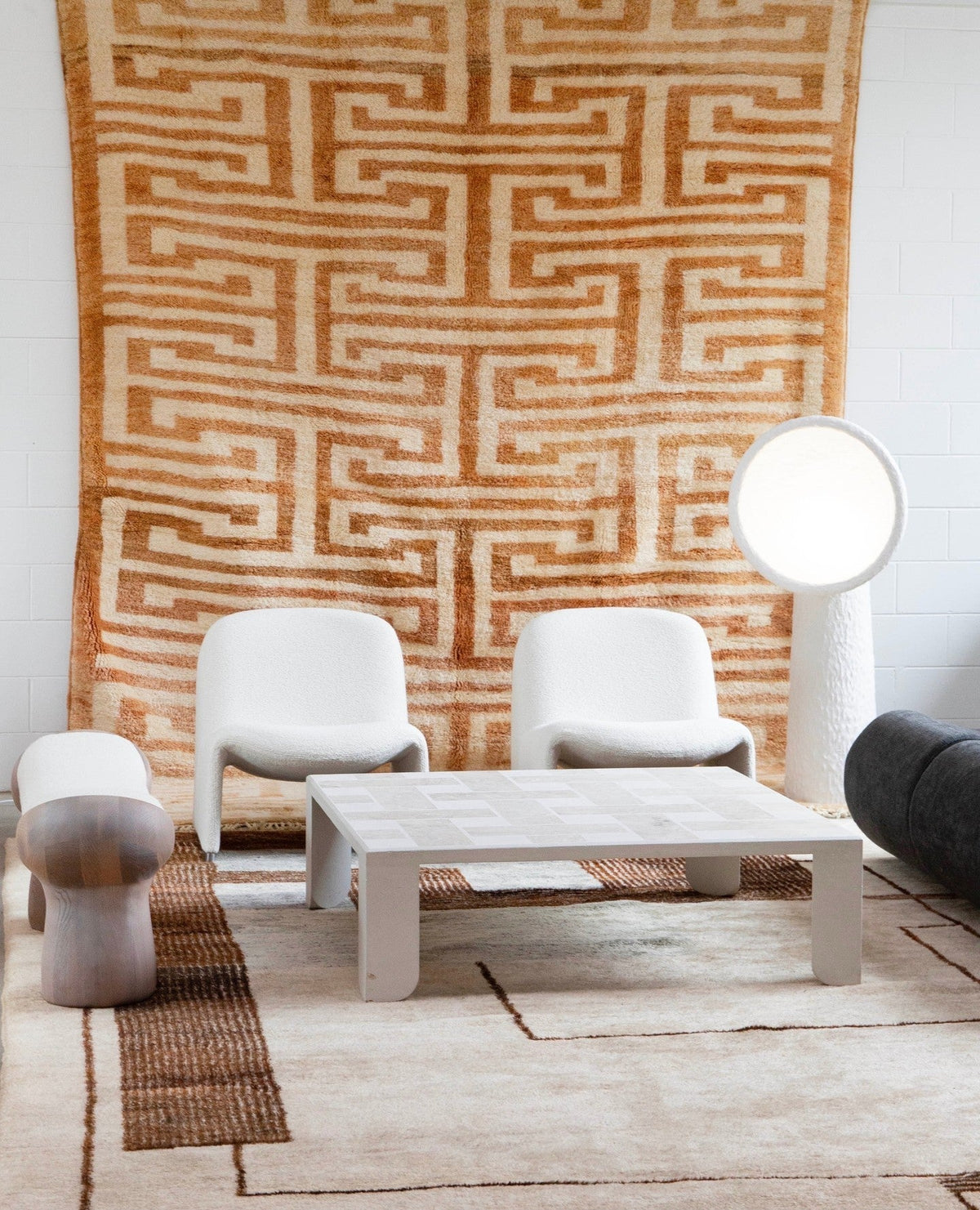 White Clérachic floor lamp beside a pair of white armchairs and a square coffee table, with a large woven rug on the wall.