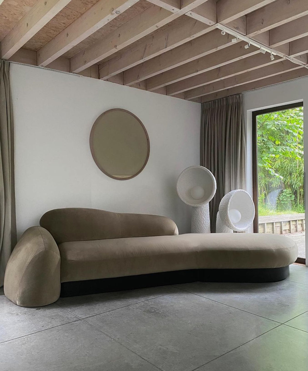 White Clérachic floor lamp beside a curved olive sofa, with a round mirror on the wall and a timber-beamed ceiling.