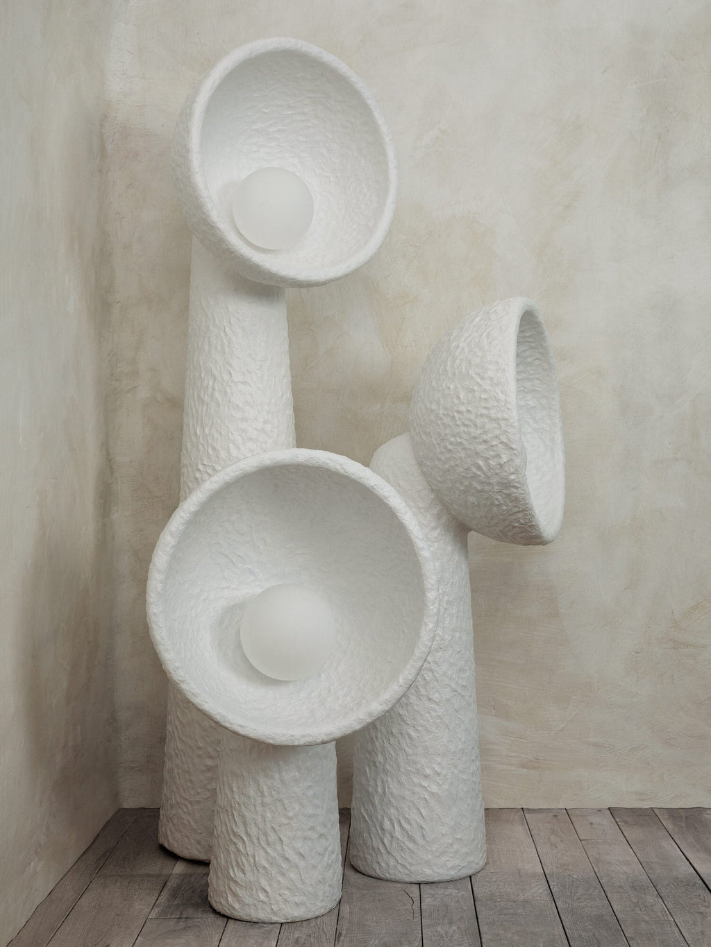 Three white textured Clérachic floor lamps grouped in a corner, the bowl shades facing different ways, on a wooden floor.