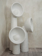Three white textured Clérachic floor lamps grouped in a corner, the bowl shades facing different ways, on a wooden floor.