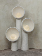Three Clérachic floor lamps glowing warm in a corner, their rough white bowls lit from inside above a wooden floor.