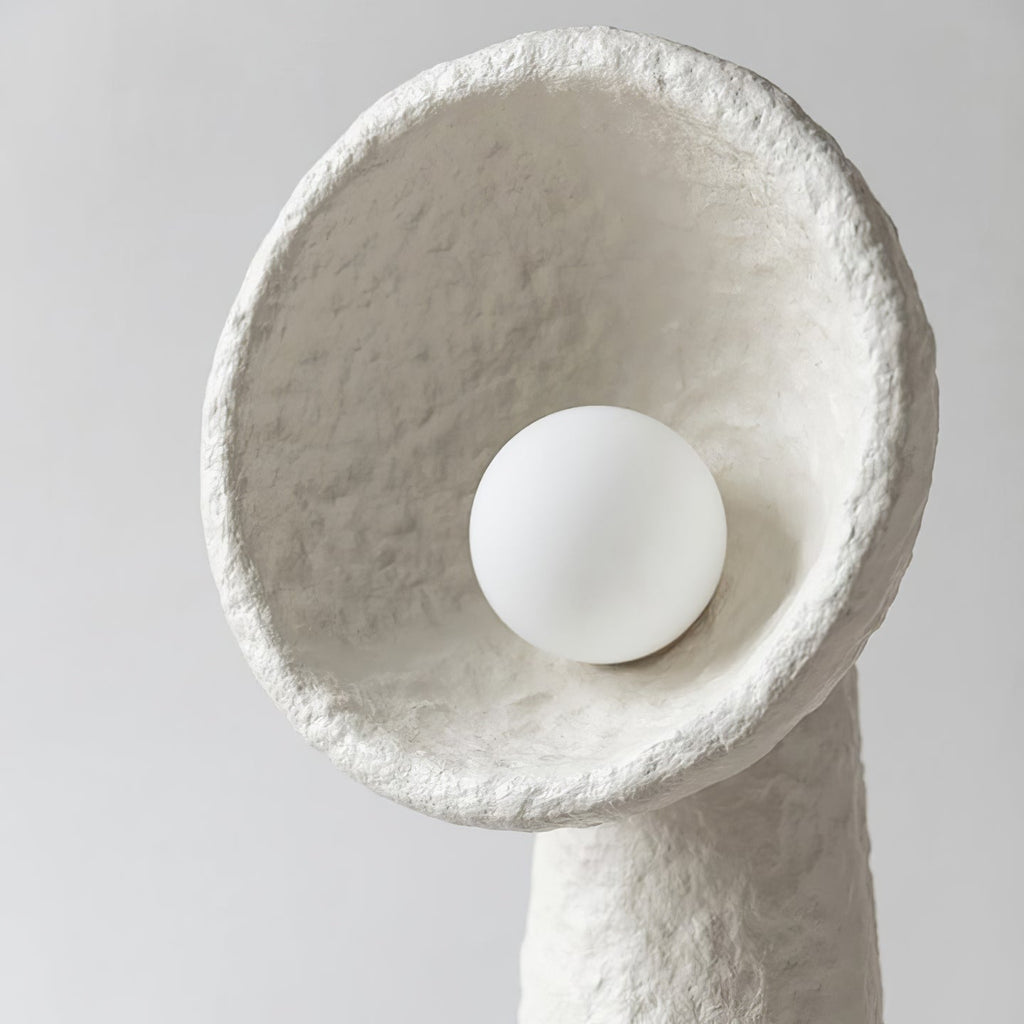 Close view of the round white bulb sitting inside the rough-textured bowl shade of this Clérachic floor lamp.