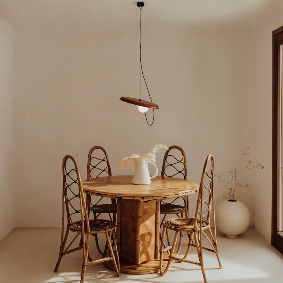 Clérachic pendant with a terracotta-toned disc and opal globe hung over a round wooden dining table with rattan chairs.