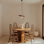 Clérachic pendant with a terracotta-toned disc and opal globe hung over a round wooden dining table with rattan chairs.
