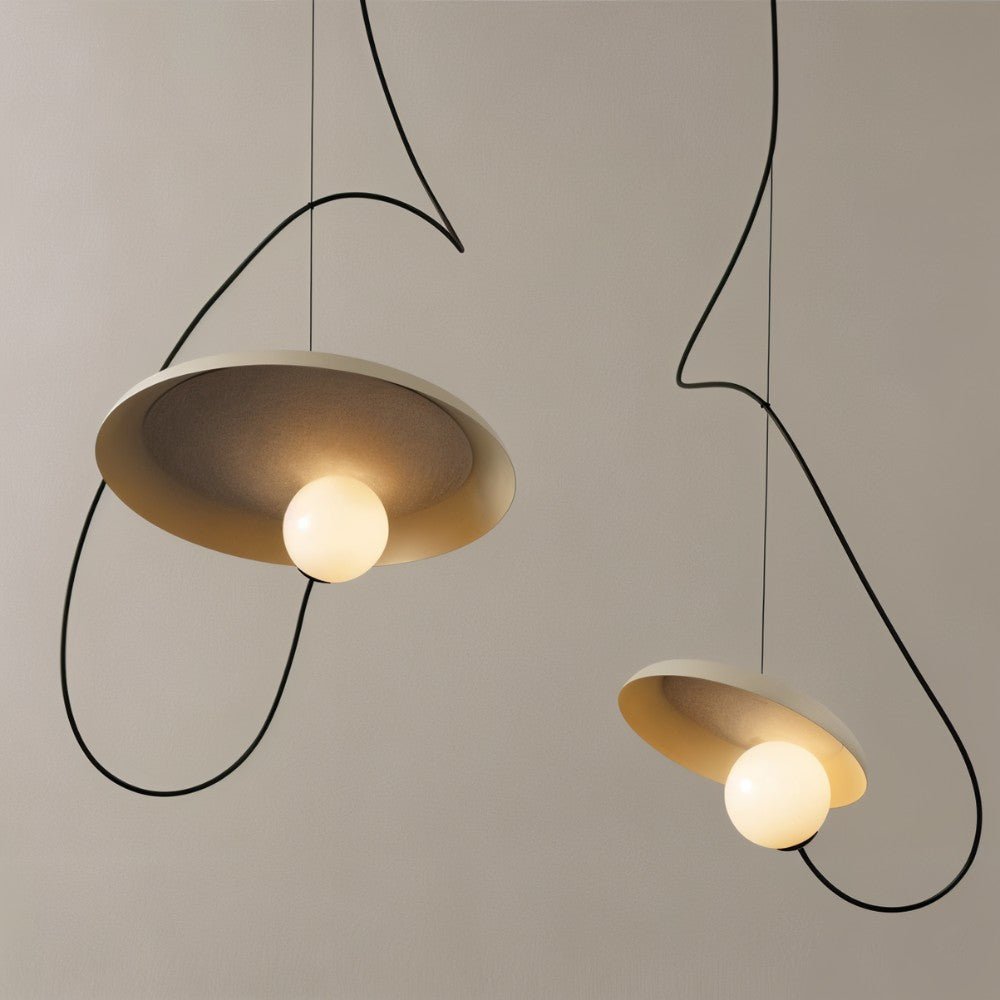 Two Clérachic cream disc pendants with glowing opal globes and looping black cords against a warm grey wall.