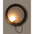 Round Clérachic wall-mounted light with a bronze rim, textured glass centre and a lit opal globe on a looping cord.