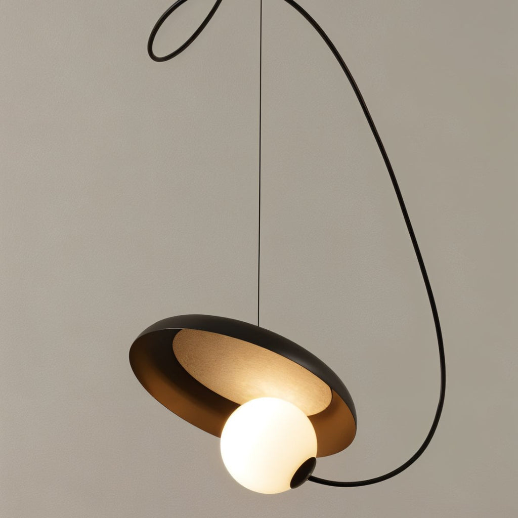 Clérachic pendant with a black disc, warm bronze inner face and a glowing opal globe, on a sweeping black cord.