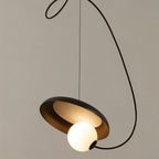 Clérachic pendant with a black disc, warm bronze inner face and a glowing opal globe, on a sweeping black cord.