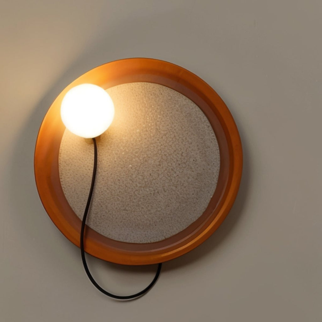Round Clérachic wall light with an orange-toned rim, a textured glass centre and an opal globe on a looping cord.