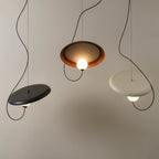 Three Clérachic disc pendants in black, terracotta and cream hanging at different heights, each with an opal globe.