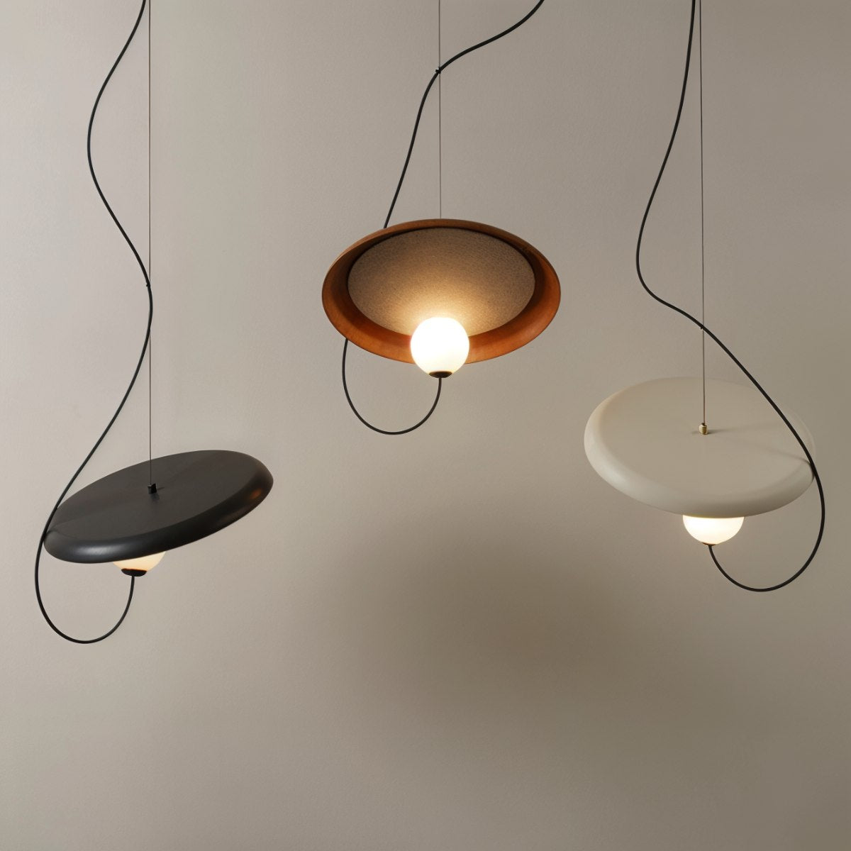 Three Clérachic disc pendants in black, terracotta and cream hanging at different heights, each with an opal globe.