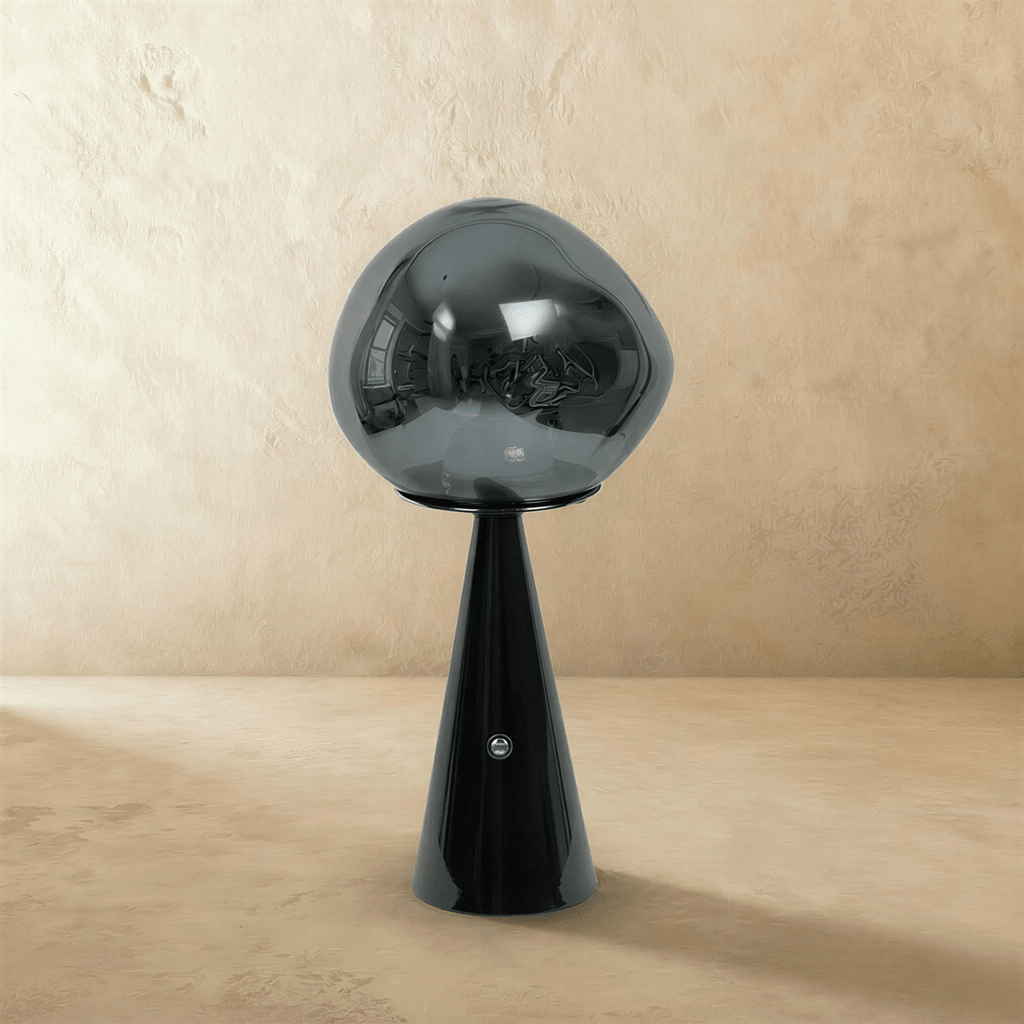 Clérachic table lamp with a smoky grey distorted glass shade on a glossy black conical base, switched off on a plaster backdrop.