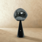 Clérachic table lamp with a smoky grey distorted glass shade on a glossy black conical base, switched off on a plaster backdrop.