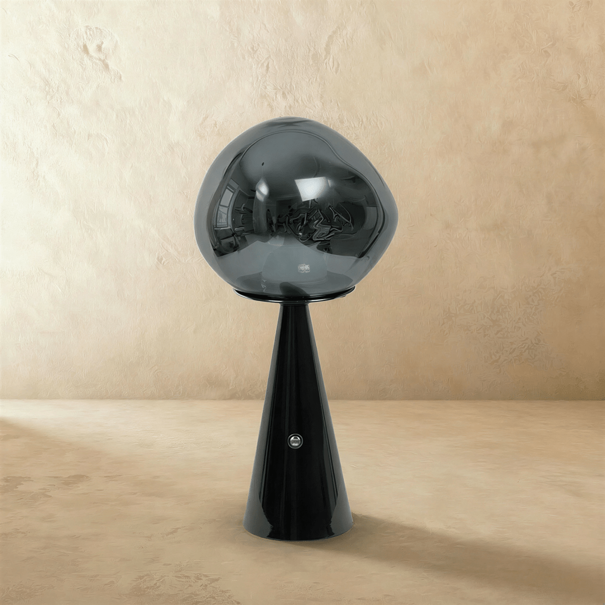 Clérachic table lamp with a smoky grey distorted glass shade on a glossy black conical base, switched off on a plaster backdrop.