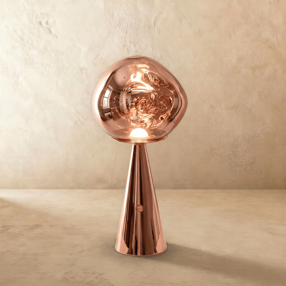 Clérachic rose gold table lamp with a mirrored, distorted glass shade lit warm on a polished copper-toned conical base.