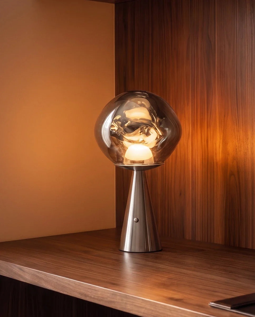 Clérachic chrome silver table lamp with a distorted glass shade lit warm on a walnut shelf against a wood-panelled wall.