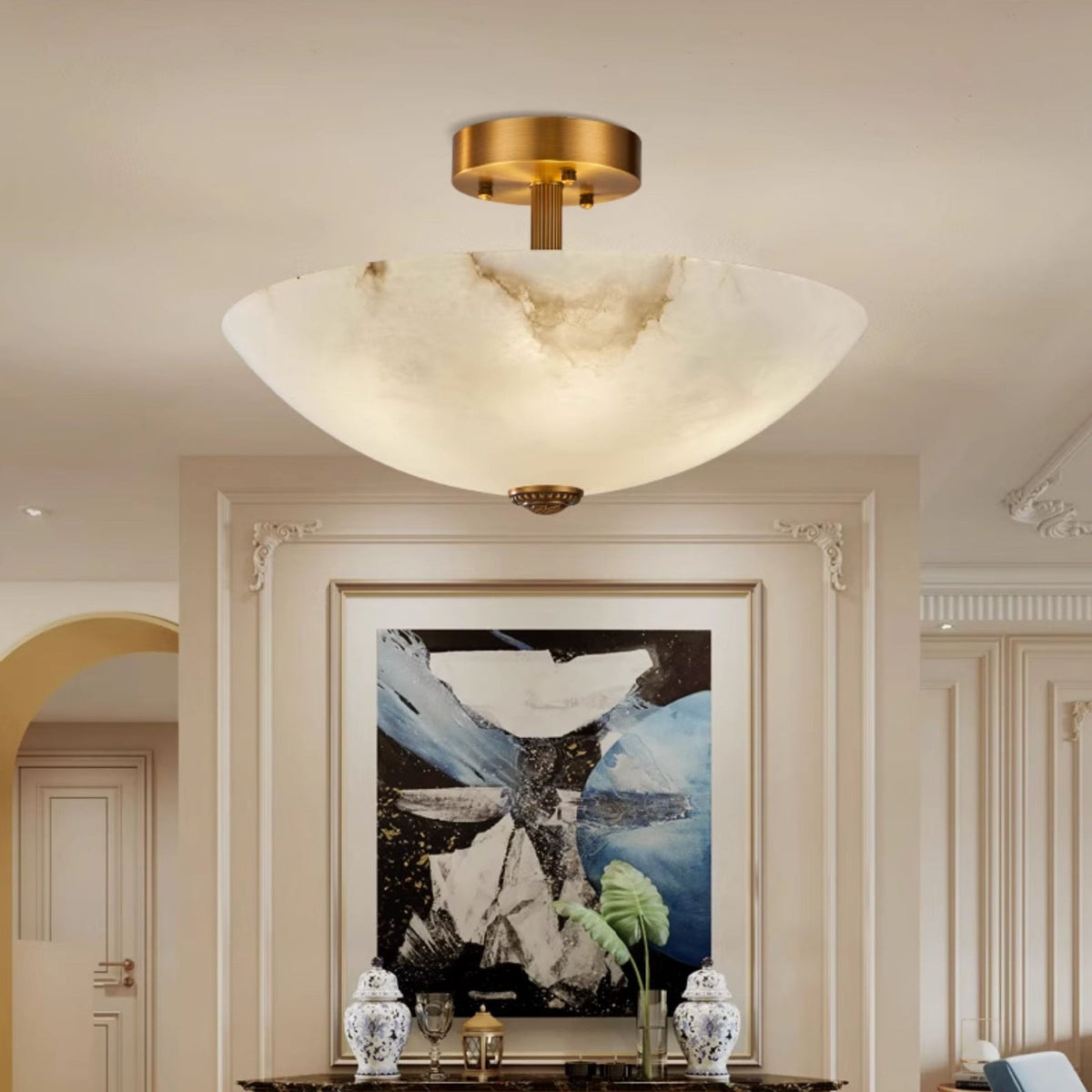 A Clérachic alabaster ceiling light glowing in a hallway, with a large abstract painting and blue-and-white vases beneath it.