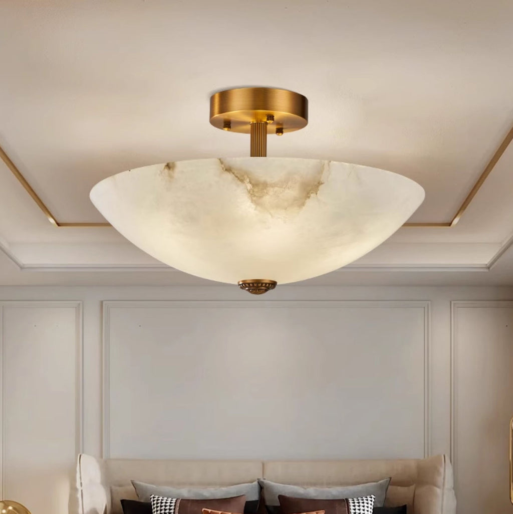 Seen from below, this Clérachic alabaster dome hangs in a cream room with a gold-edged ceiling recess and a grey sofa behind.