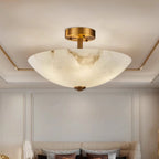 Seen from below, this Clérachic alabaster dome hangs in a cream room with a gold-edged ceiling recess and a grey sofa behind.