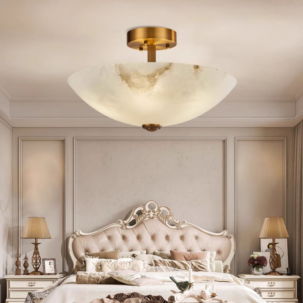 Warm light through the alabaster of this Clérachic ceiling light, hung over a carved, tufted bed with a lamp on each side table.