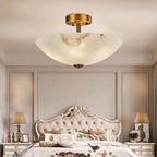 Warm light through the alabaster of this Clérachic ceiling light, hung over a carved, tufted bed with a lamp on each side table.