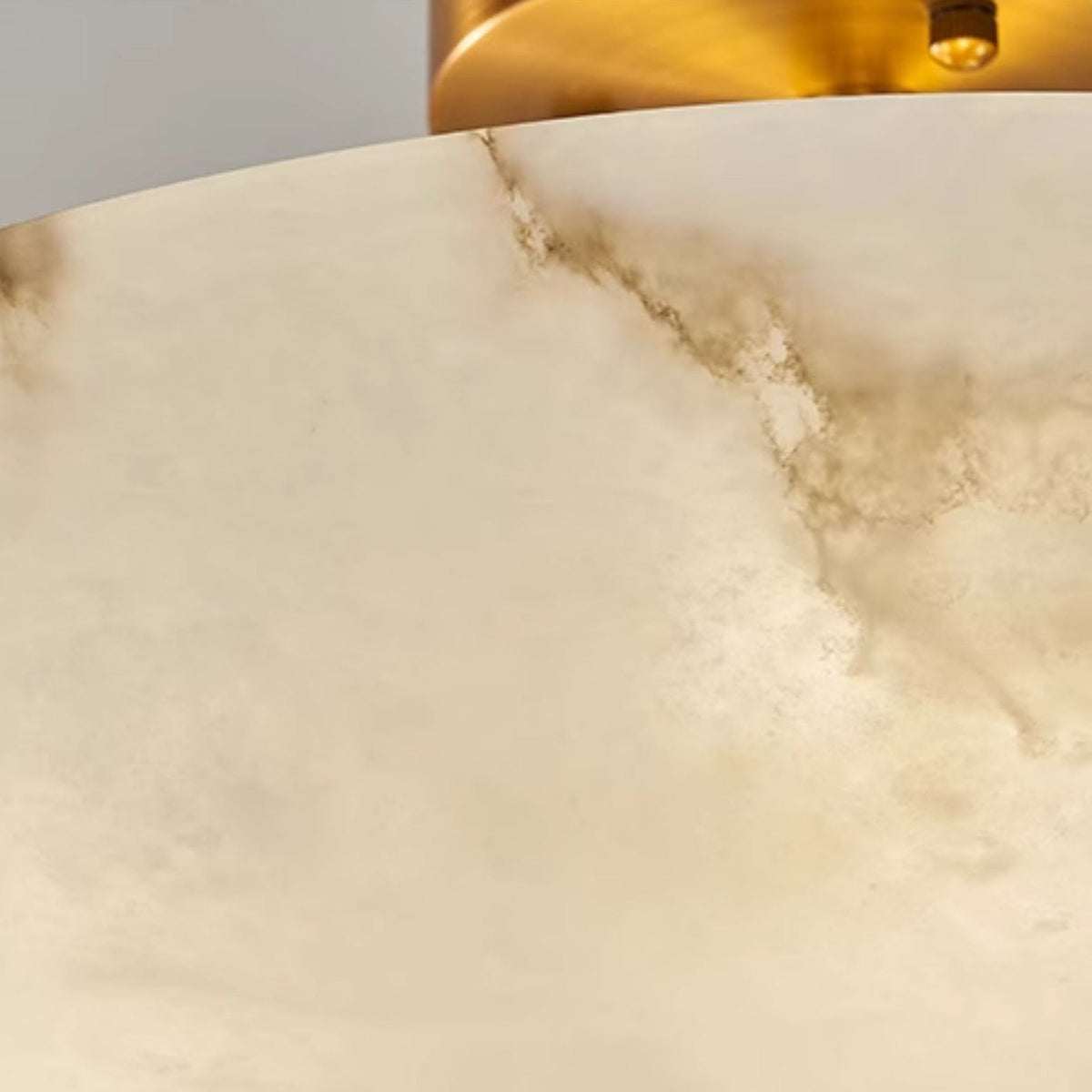 Close view of the cloudy alabaster surface on this Clérachic ceiling light, with the brass canopy edge at the top.