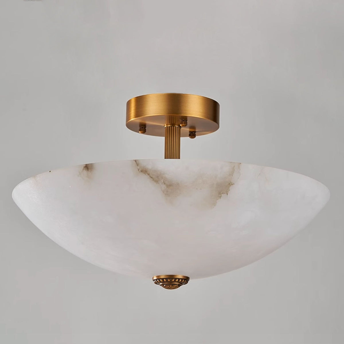 Low, close angle on this Clérachic alabaster dome, showing its deep bowl, fluted brass stem and finial against grey.