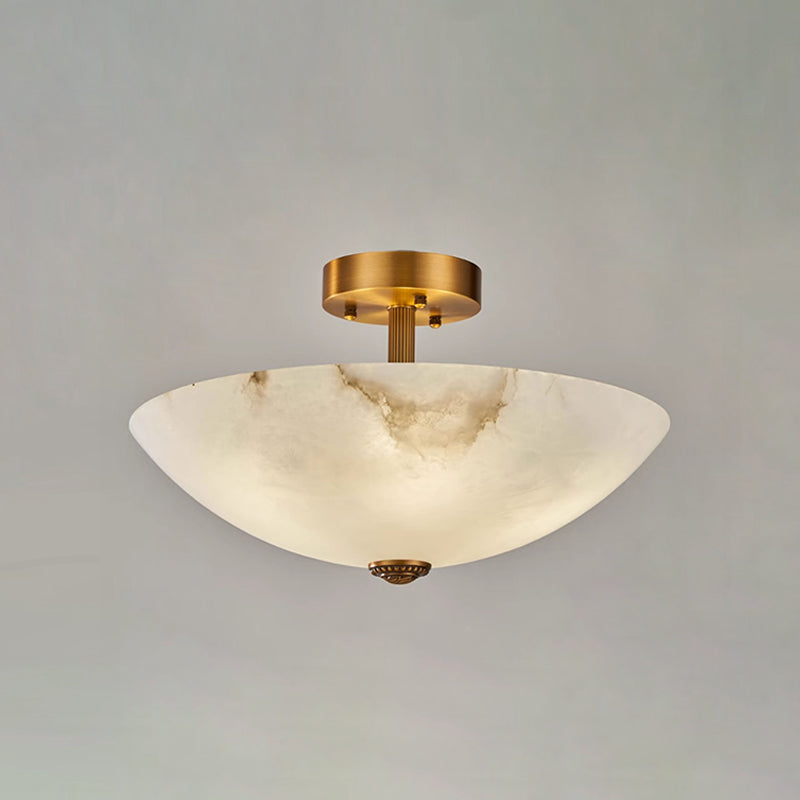 Front view of this Clérachic ceiling light on grey, the alabaster bowl glowing softly under its short brass stem.