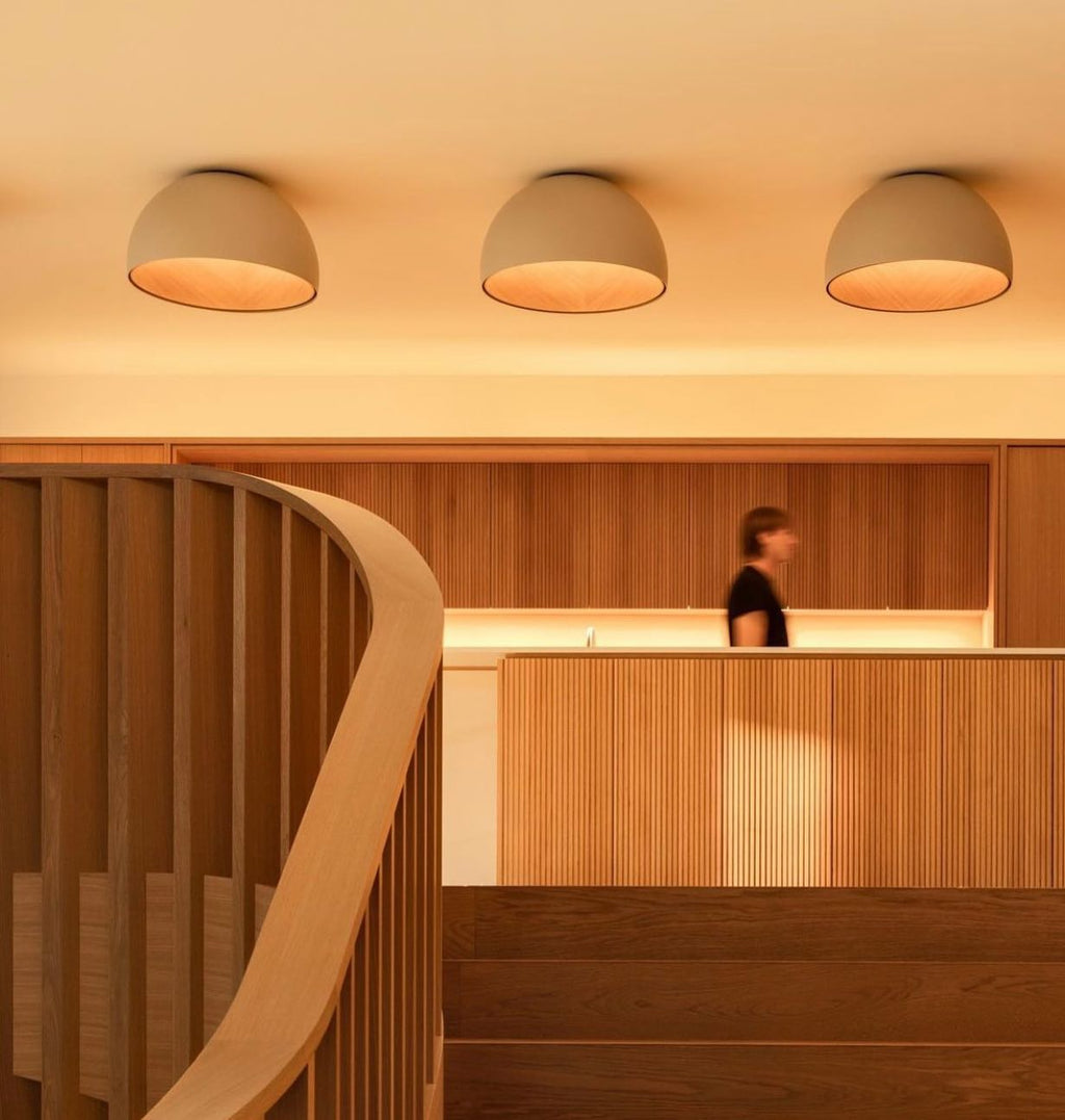 Three grey-white Clérachic dome ceiling lights in a row, lit warm above a timber reception counter and a curved wooden handrail.