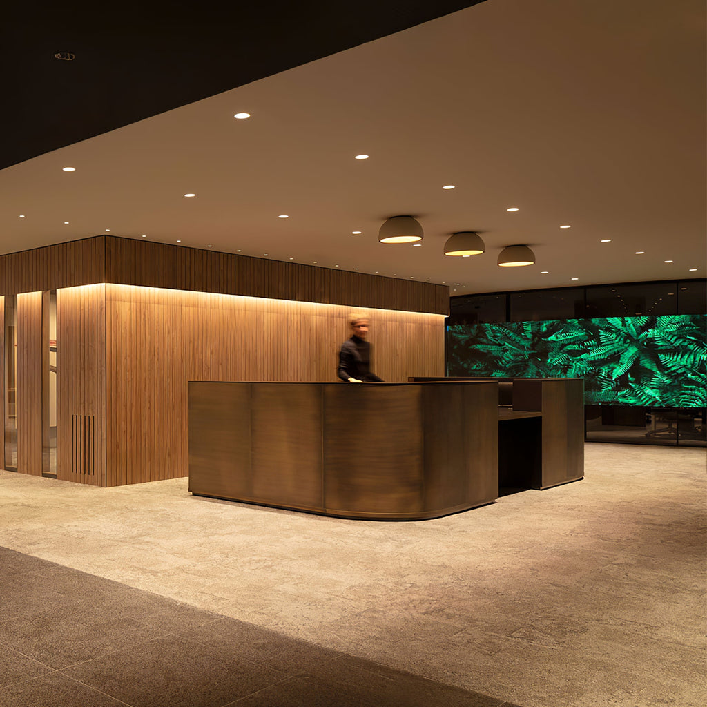 Three small Clérachic dome ceiling lights in a row above a bronze reception desk, with a timber-slatted wall and a green screen behind.