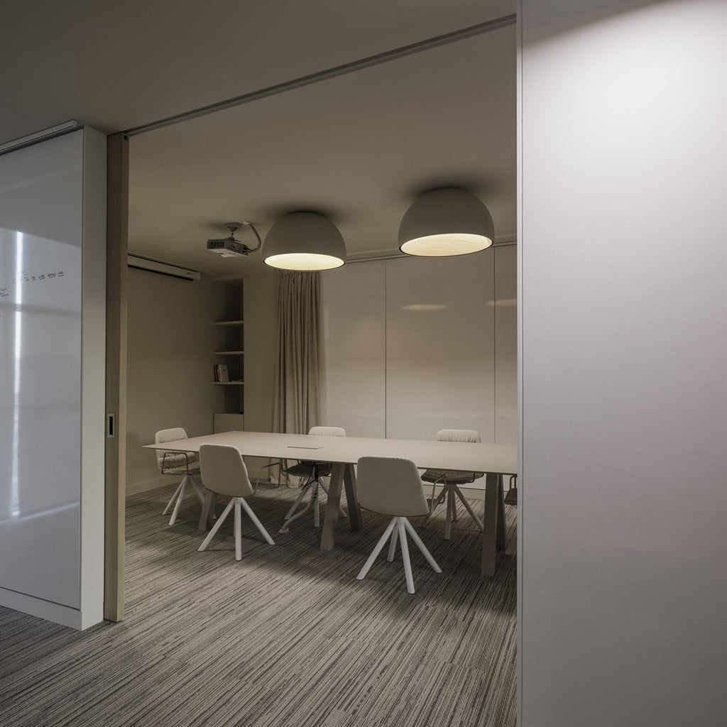 Two white Clérachic dome ceiling lights lit over a meeting table with white chairs, seen through an open sliding glass door.