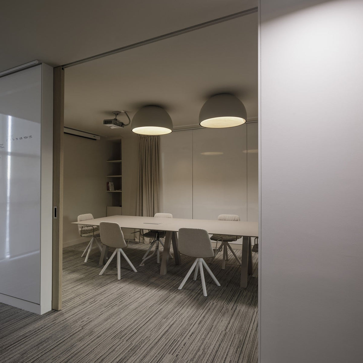 Two white Clérachic dome ceiling lights lit over a meeting table with white chairs, seen through an open sliding glass door.