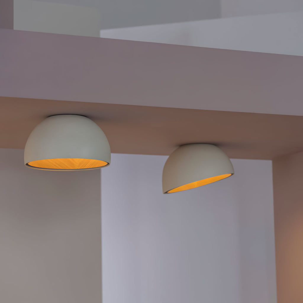 Two pale grey Clérachic dome ceiling lights angled in a corner, lit warm so the oak interior shows against white walls.