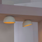 Two pale grey Clérachic dome ceiling lights angled in a corner, lit warm so the oak interior shows against white walls.